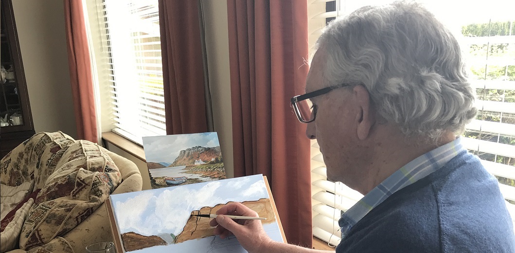Barry White painting a landscape with white, blue and brown paint on his canvas which sits in front of a window