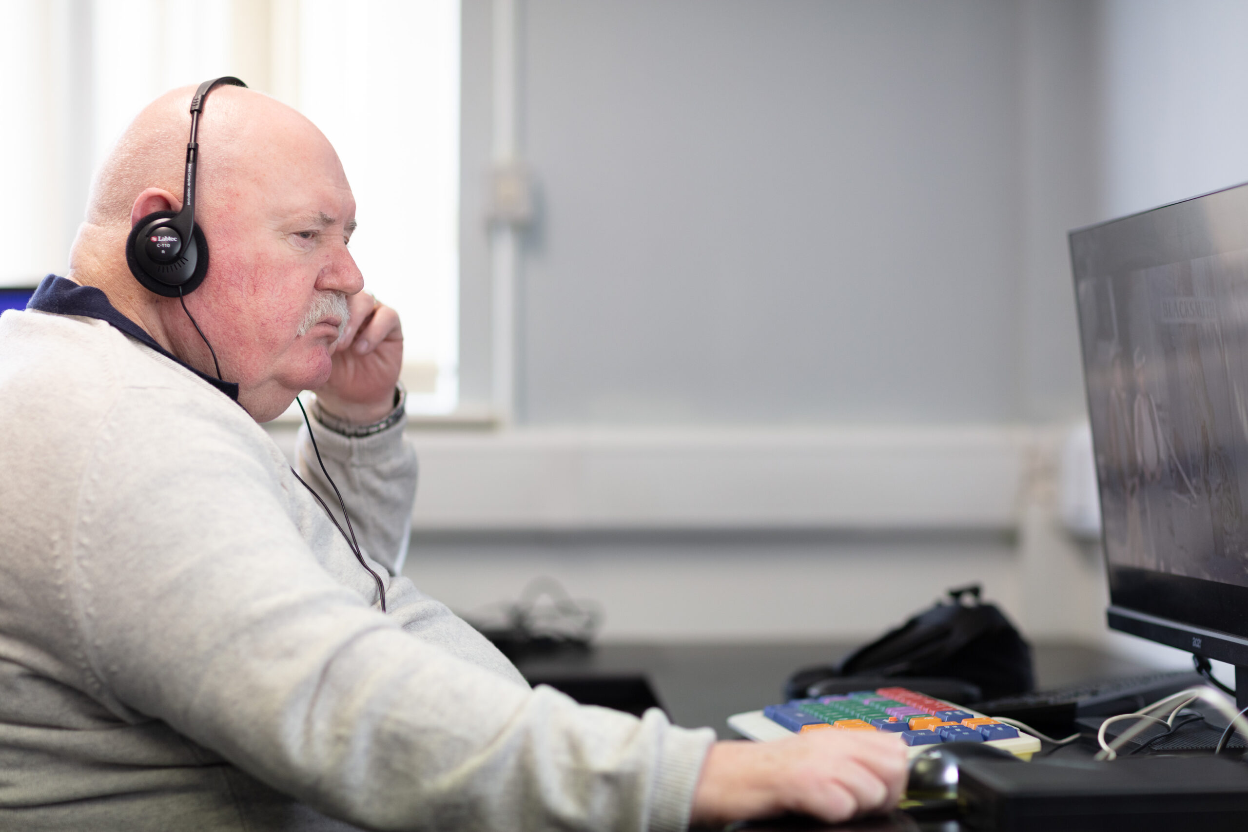 An NCBI service user sitting at a computer using accessibility features as he wears headphones